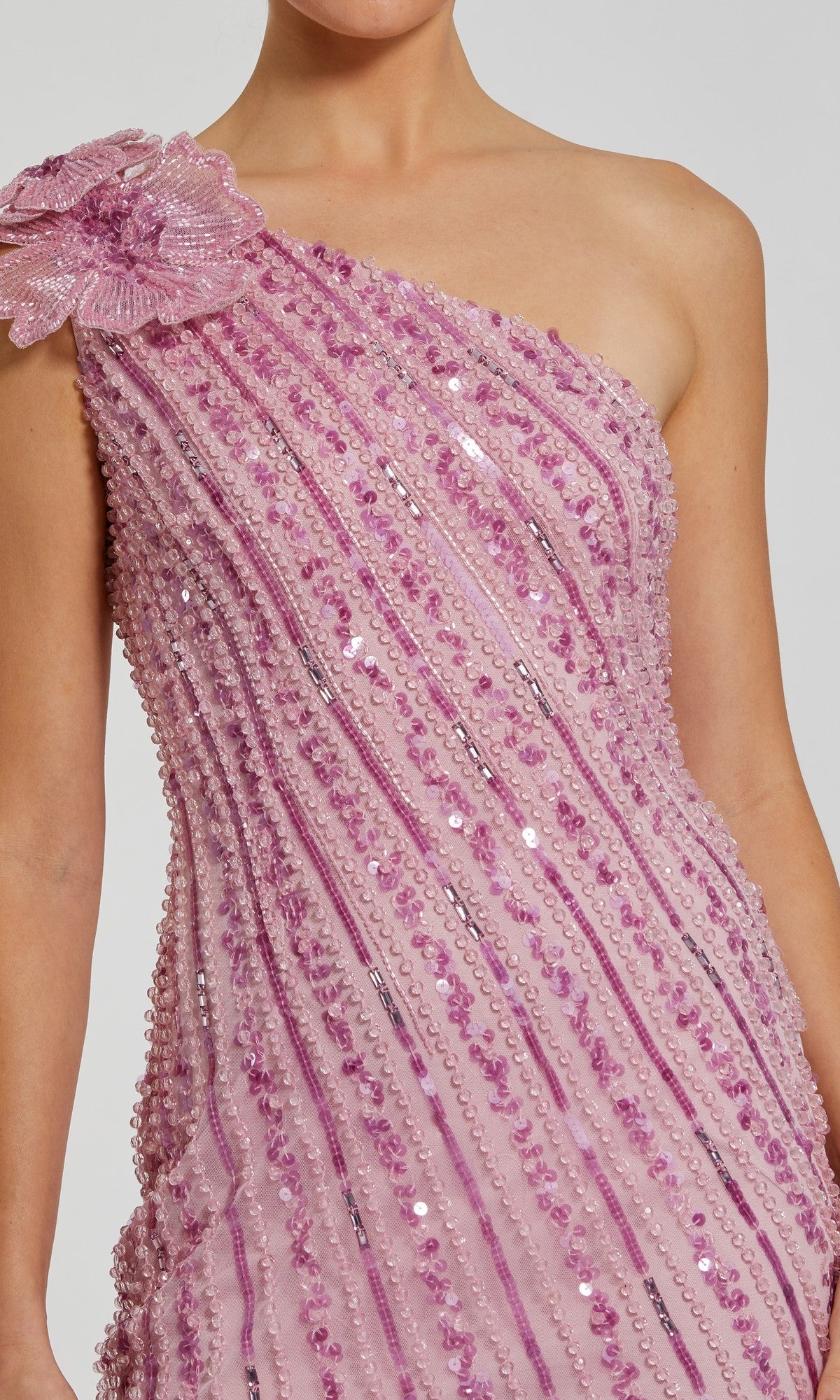 Person wearing the Mac Duggal 94221 Long Formal Dress in light pink, featuring sequin and bead detailing, a large fabric flower on one shoulder, and elegant diagonal accents.